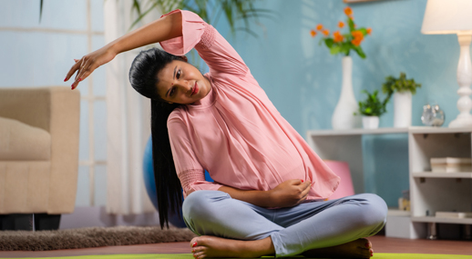 A pregnant woman stretching in a seated yoga pose at home